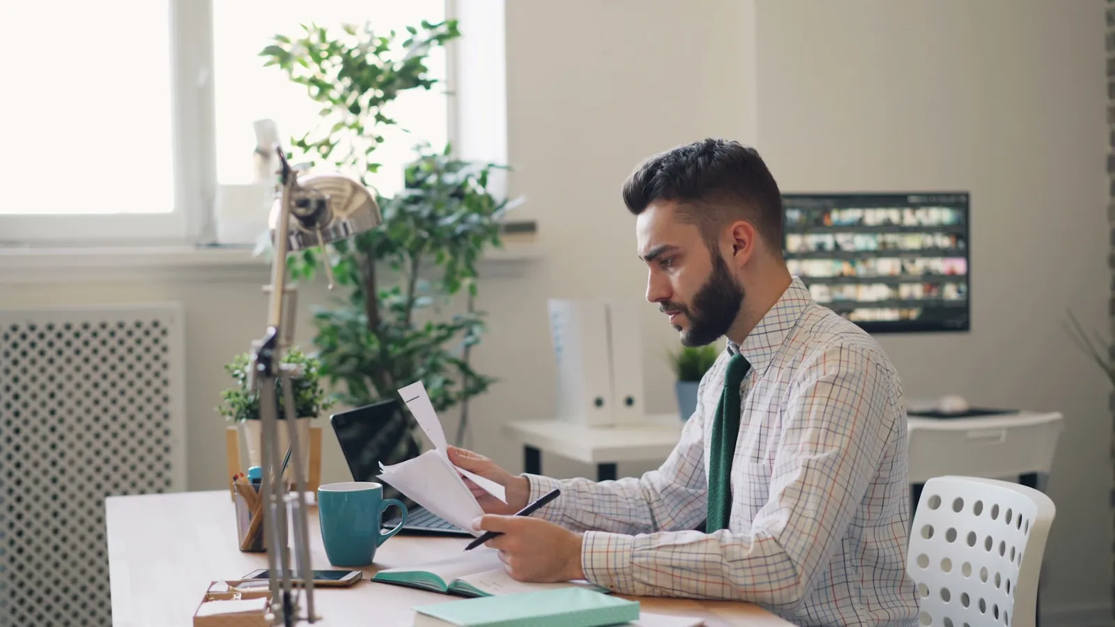 Un professionnel lit des documents à son bureau, dans un open space lumineux